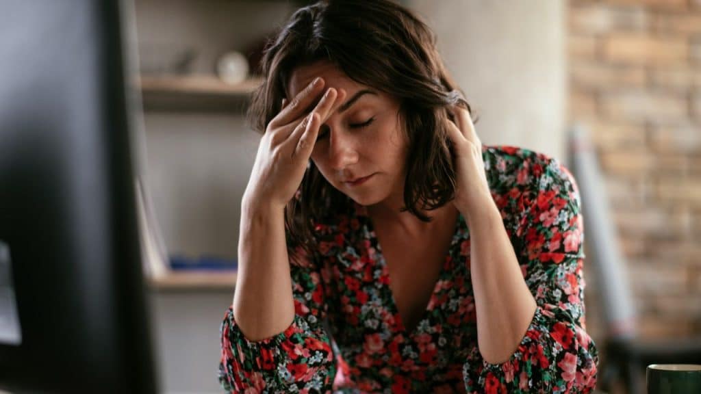 Woman in floral dress sitting at a desk, holding her head in distress.