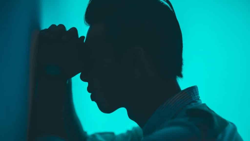 A silhouette of a person sitting in blue light, holding their hands to their head.