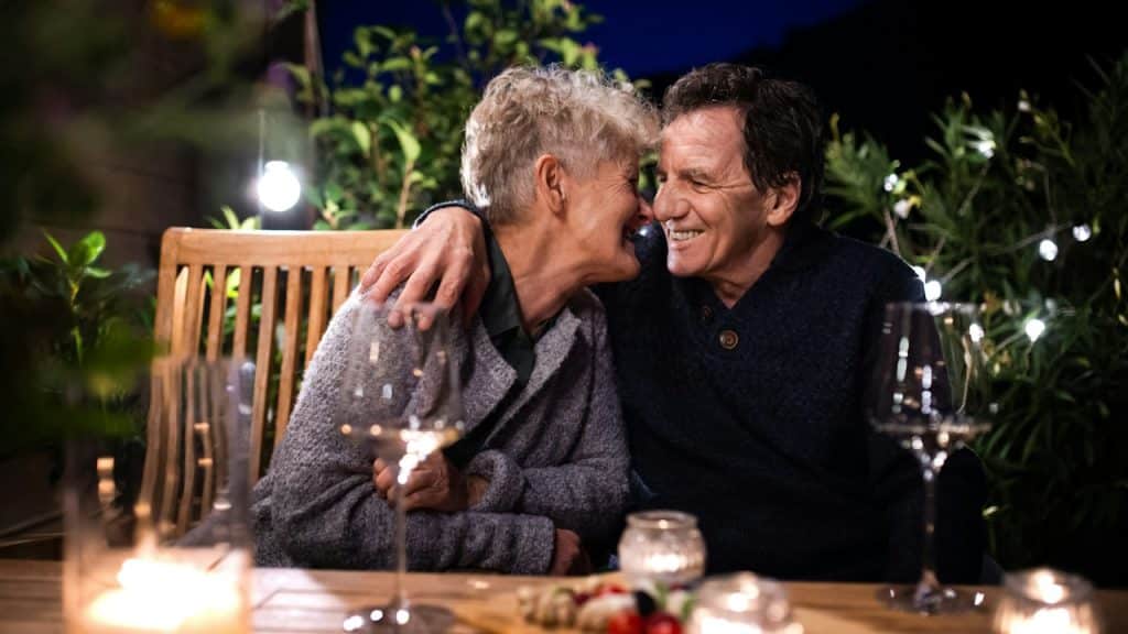 A young couple hugging while sitting at a table with glasses of wine on it.