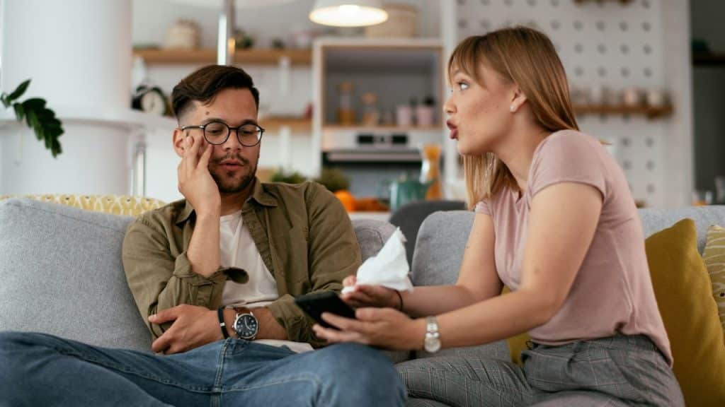 A man sits with a pained expression next to an angry, talking woman.