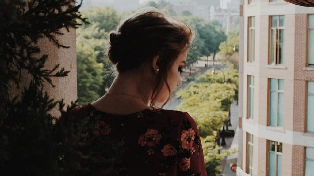 A woman standing on a balcony looking down toward the street below.