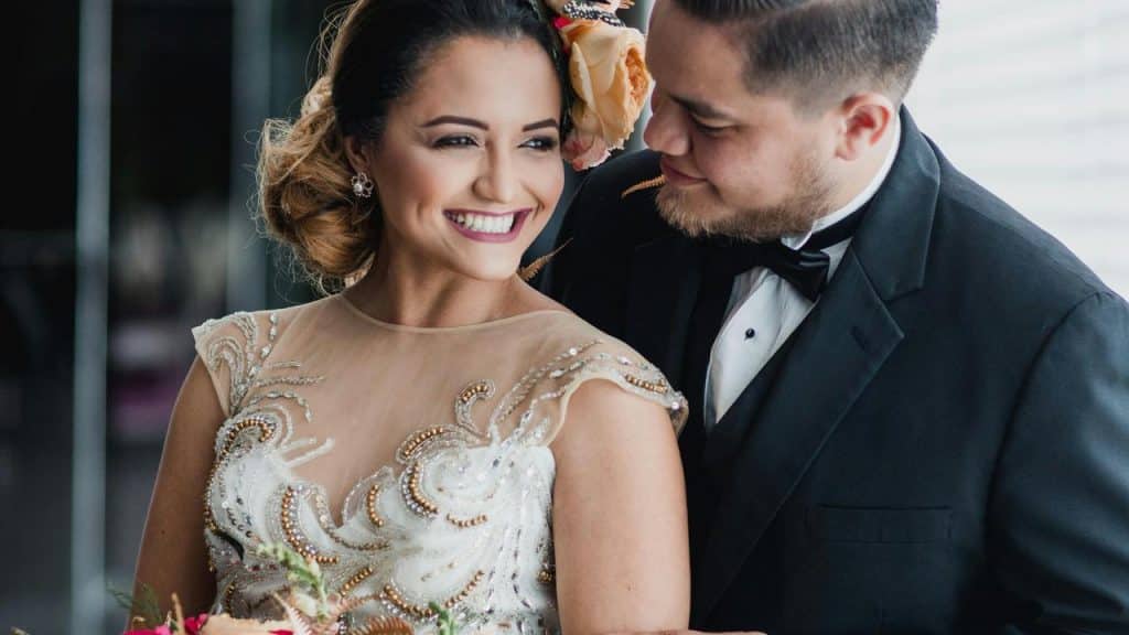 A smiling bride and groom stand close together, with the groom looking lovingly at the bride.