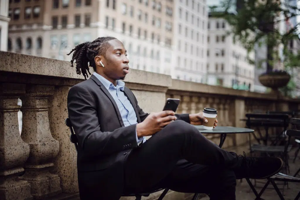 Pensive black businessman resting in outdoor cafe with smartphone and takeaway coffee