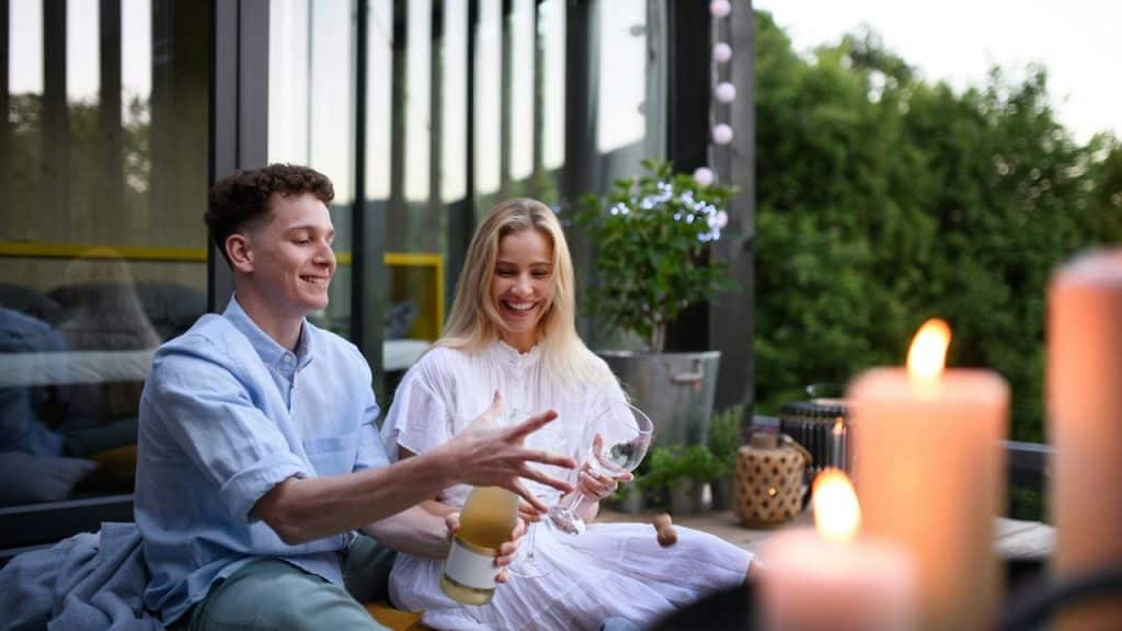 A happy couple popping a champagne bottle on an outdoor patio.