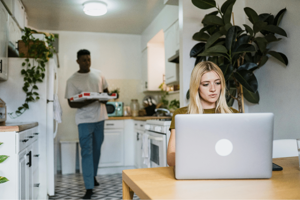 Woman Working with Laptop While Man Holding Pizza
