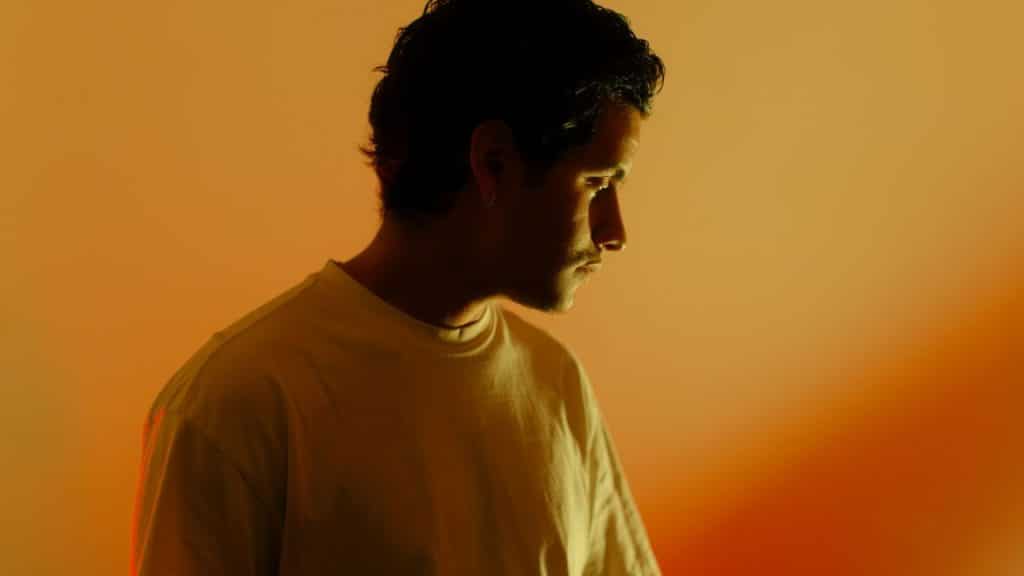 A thoughtful man is illuminated by warm, orange light, looking down and away.