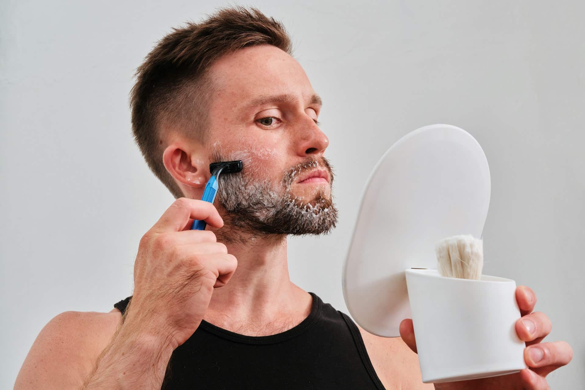 A man shaving in front of a hand mirror.