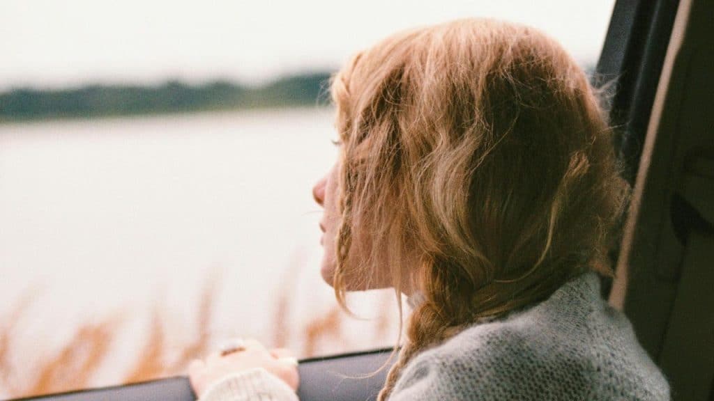 A woman looking out of a car window toward a lake.