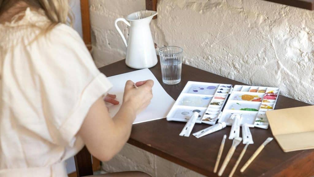 A person painting at a table with art supplies.