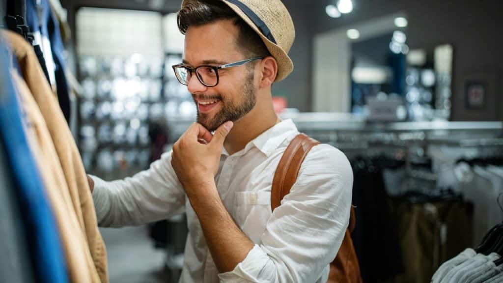 Smiling man in a straw hat and glasses shopping for clothes.