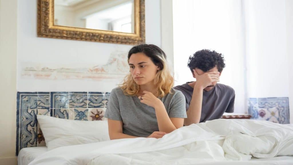 A woman and a man sitting on bed looking sad