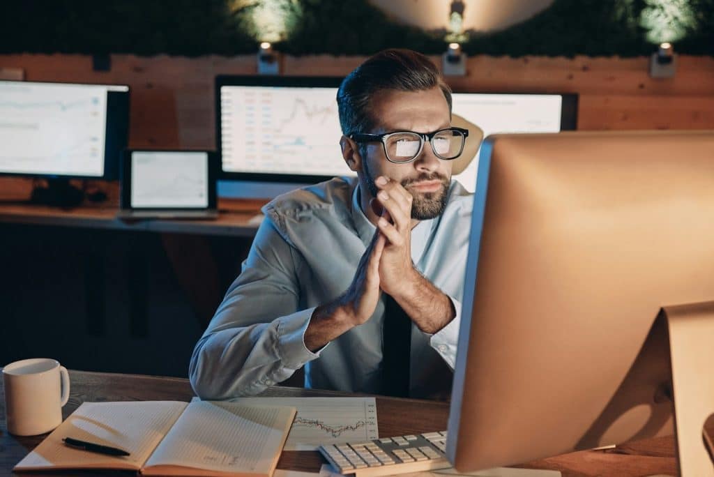 A man looking at the computer while working late in the office.