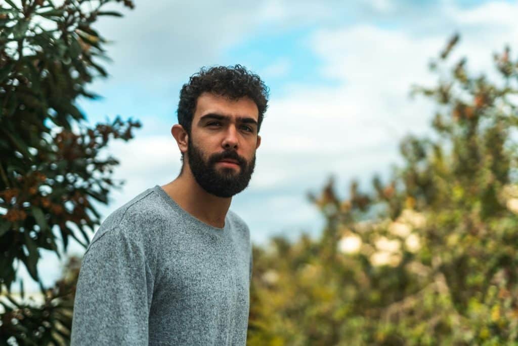 A man wearing gray shirt standing in front of a tree.