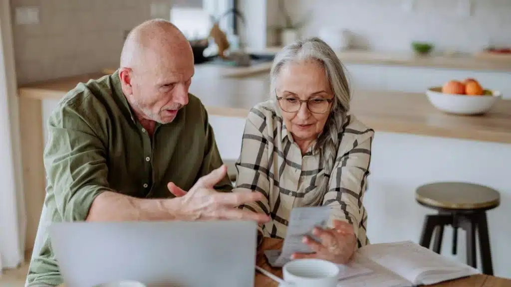 Senior couple looking at papers and a laptop in a brightly lit kitchen