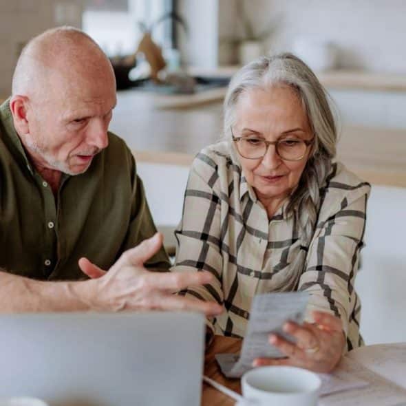 Senior couple looking at papers and a laptop in a brightly lit kitchen