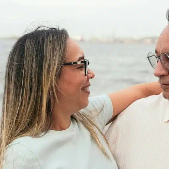 Smiling middle-aged couple in glasses outdoors, looking at each other with arm around shoulders.