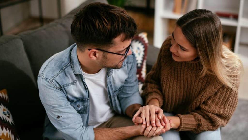 Smiling couple sitting on a couch, embracing and looking at a tablet together indoors.