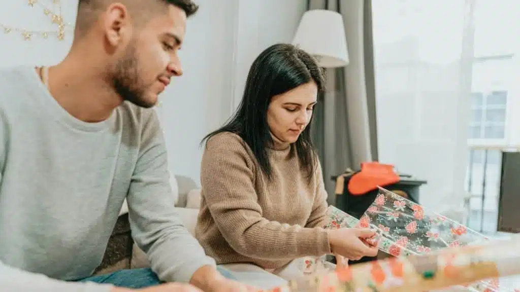 A couple is sitting side-by-side wrapping gifts, focused on the task in front of them.