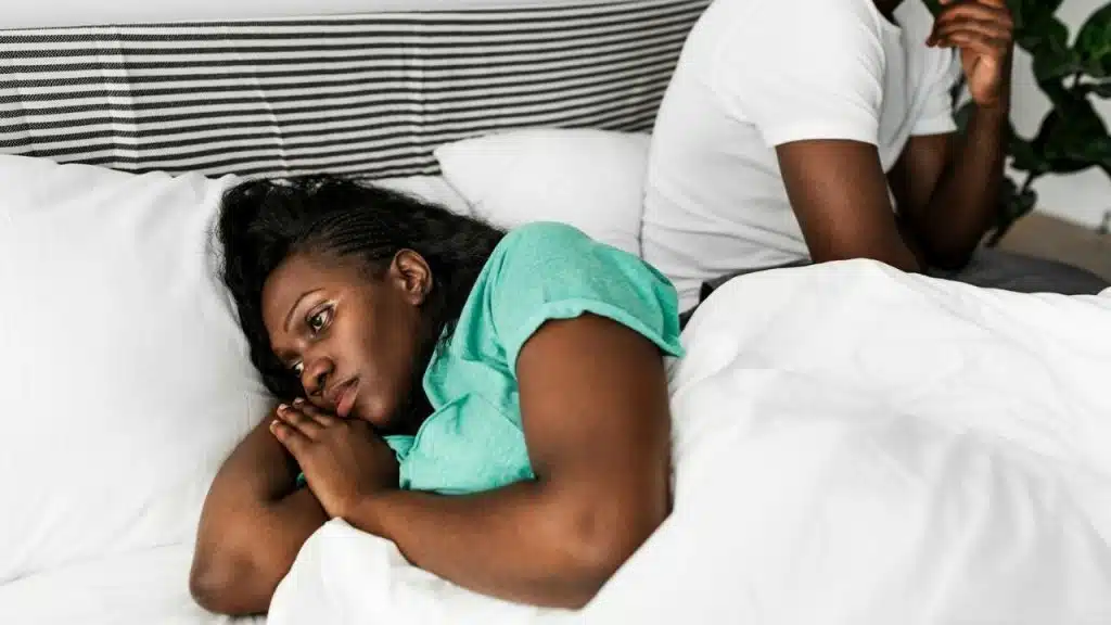 A woman lying in bed looking away from a man sitting beside her.