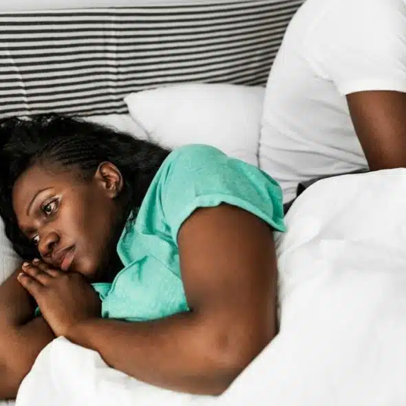 A woman lying in bed looking away from a man sitting beside her.
