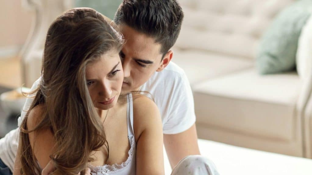 A man attempts to hug or kiss a woman who looks sad or distant in a living room.