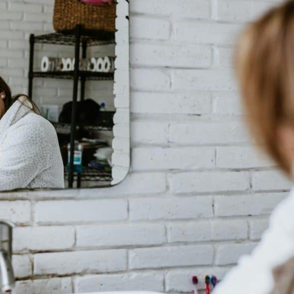 A woman in a bathroom looking at herself in the mirror while drying her hair with a towel.