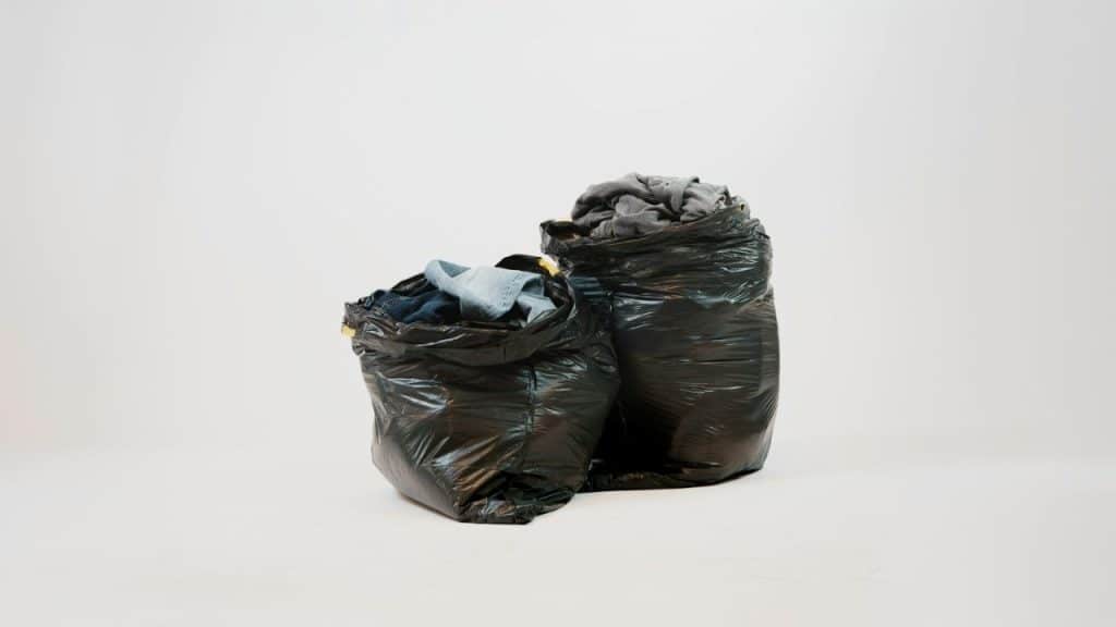 Two black trash bags, one slightly larger, filled with various articles of clothing.