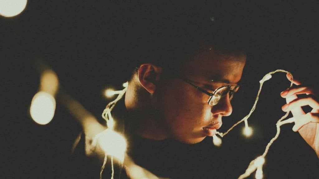 Young person in profile, wearing glasses, tangled in strands of bright white string lights.