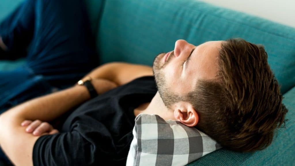 Man rests on a turquoise couch with eyes closed and an arm across his chest.