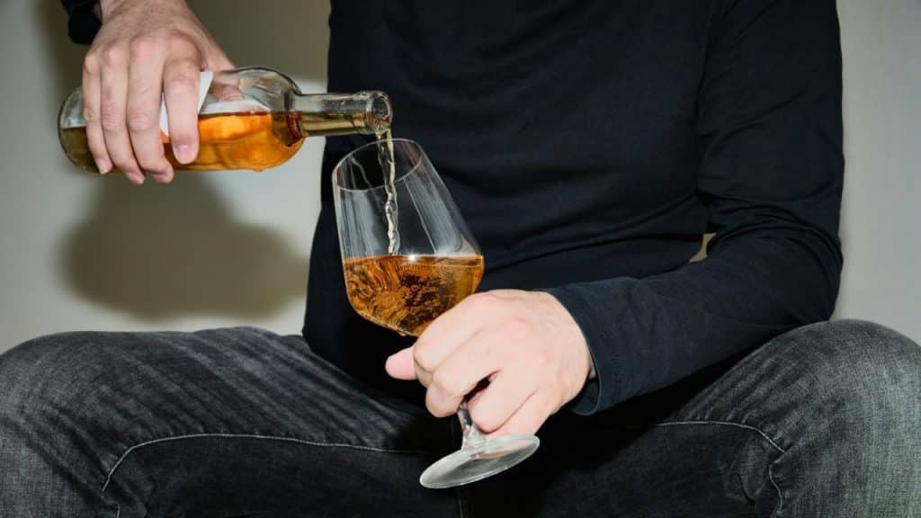 Close-up of a person pouring amber liquid from a bottle into a wide glass.