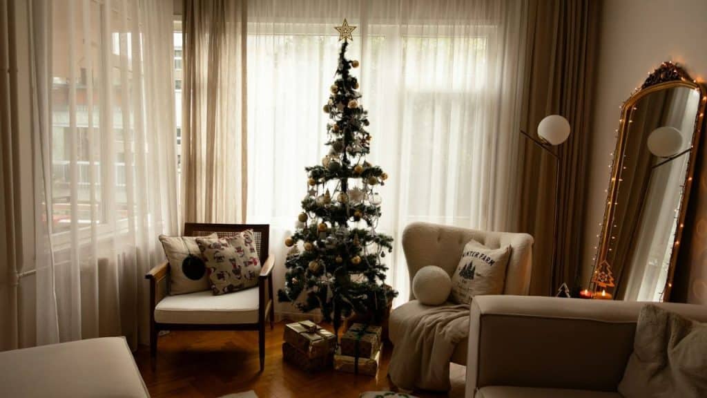 Bright living room with decorated Christmas tree, chairs, and large standing mirror.