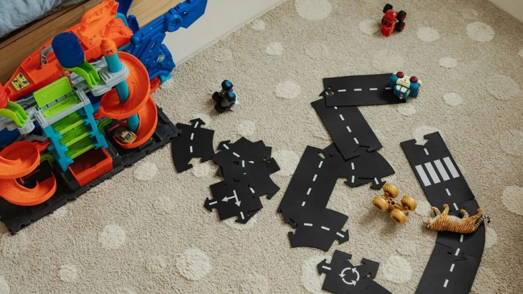 Overhead shot of toy road pieces, race cars, tiger toy, and large toy ramp on carpet.