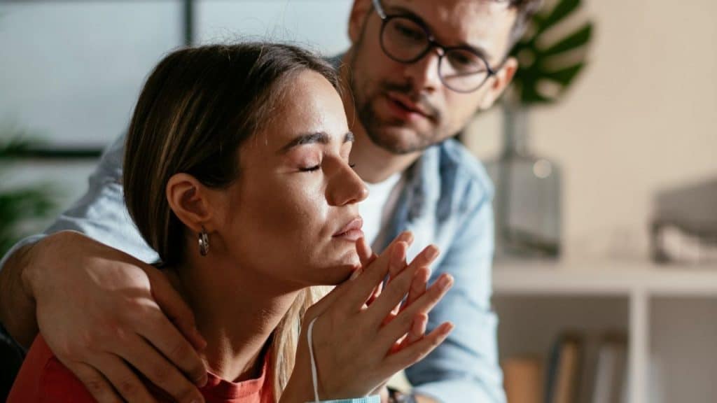 A man gently holding a woman with her eyes closed and hands clasped.