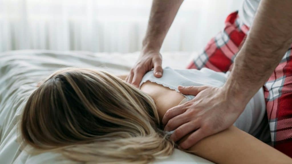 A man's hands are massaging a woman's shoulders and back on a bed.