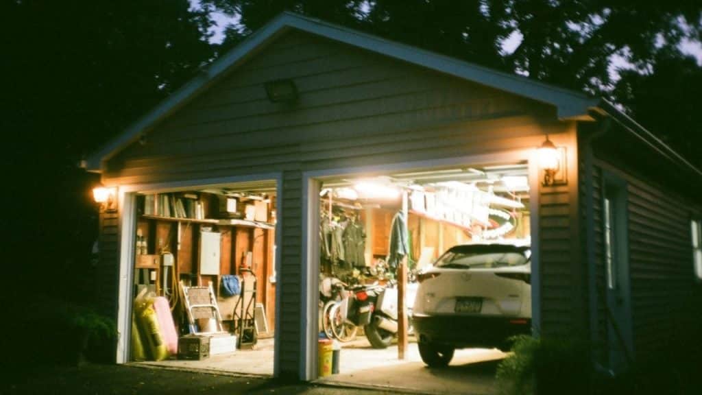 Two-car garage at night with both doors open, showing storage, a motorcycle, and a car.