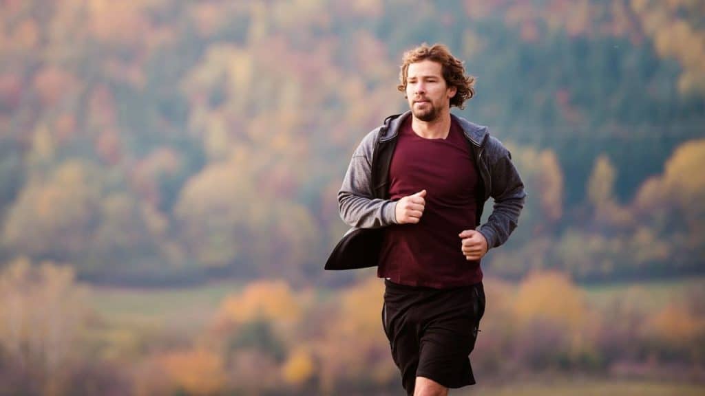 Man running outside in athletic wear with an out-of-focus background of autumn trees.