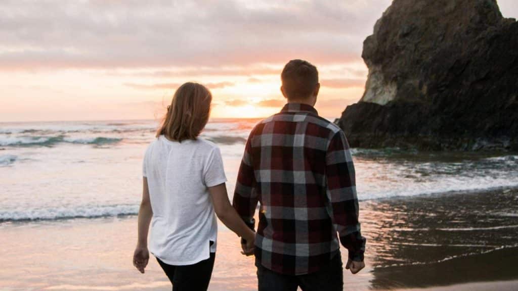 A couple holding hands while standing on the beach at sunset.