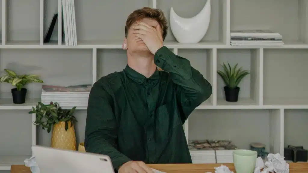 A man sitting at a desk with his hand covering his face in frustration.