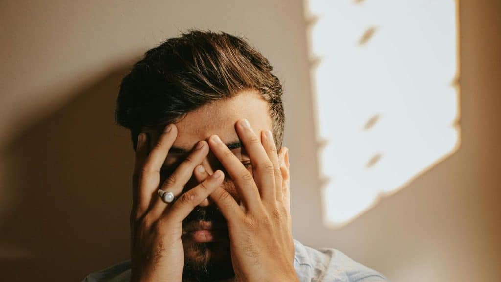 A person covering their face with both hands in soft indoor light.
