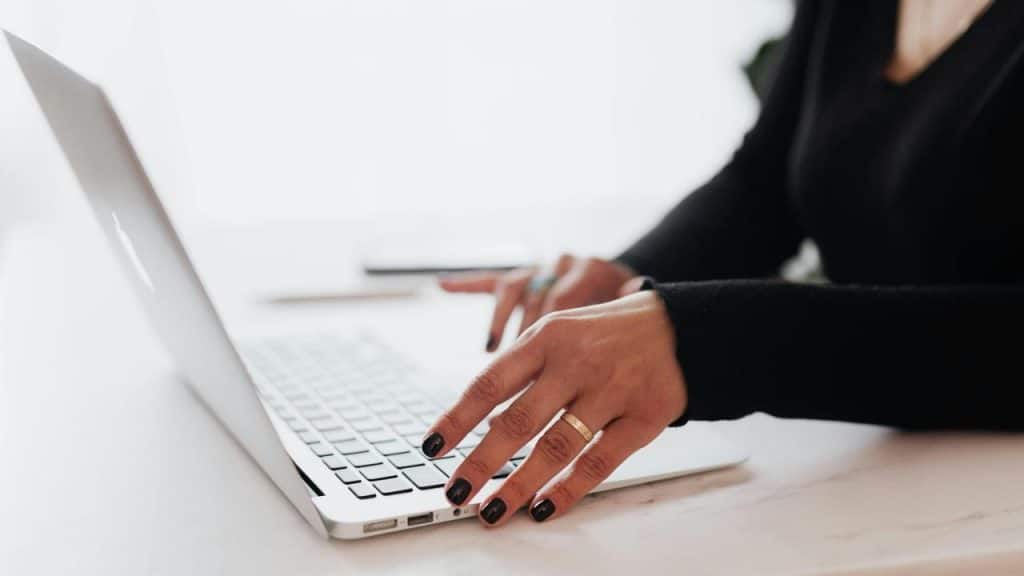 A person typing on a laptop with black-polished nails.