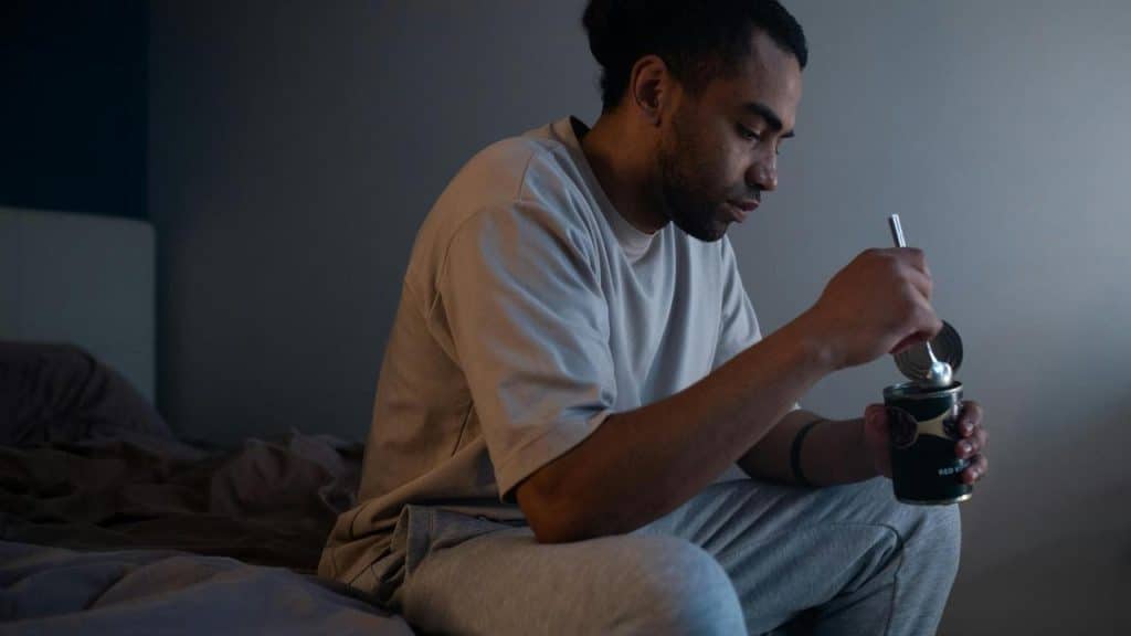 A person sitting on a bed eating from a container with a spoon.