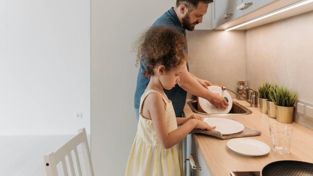 A man and a child washing and drying dishes together in a kitchen.