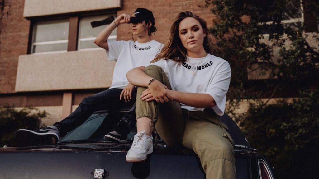 A man and a woman sitting on the hood of a car.