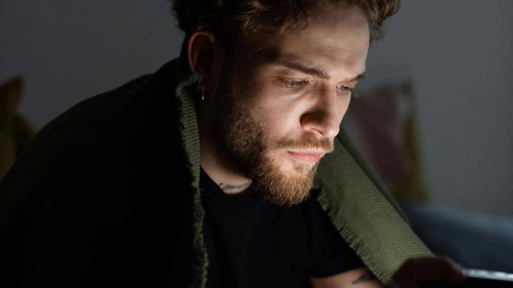 A person wrapped in a blanket looking intently at a lit screen.