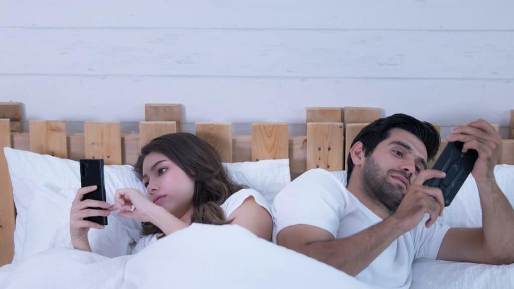 A couple in bed, both looking at their phones.