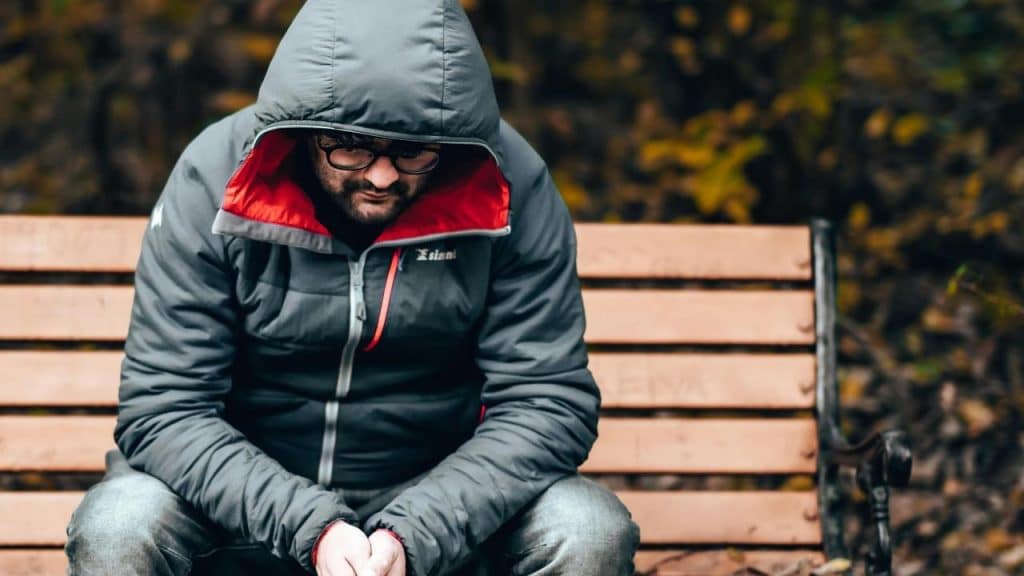 A person in a hooded jacket sitting on a bench with their head lowered.