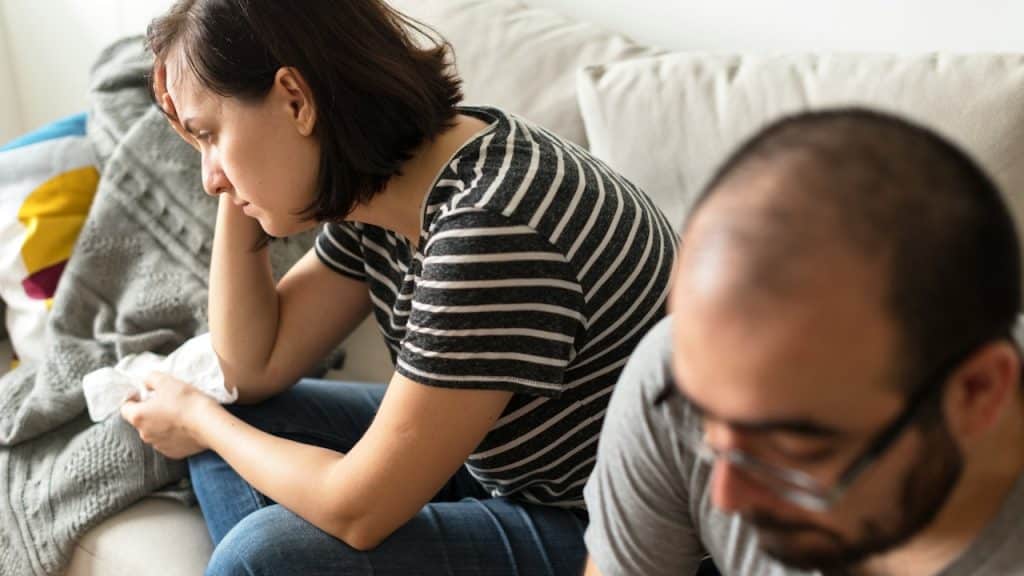Woman looking distressed, man out of focus in foreground.