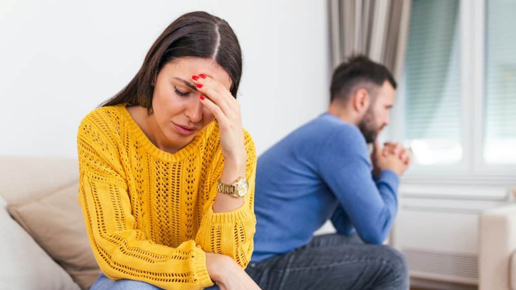 Woman looking sad on couch, man out of focus in foreground.