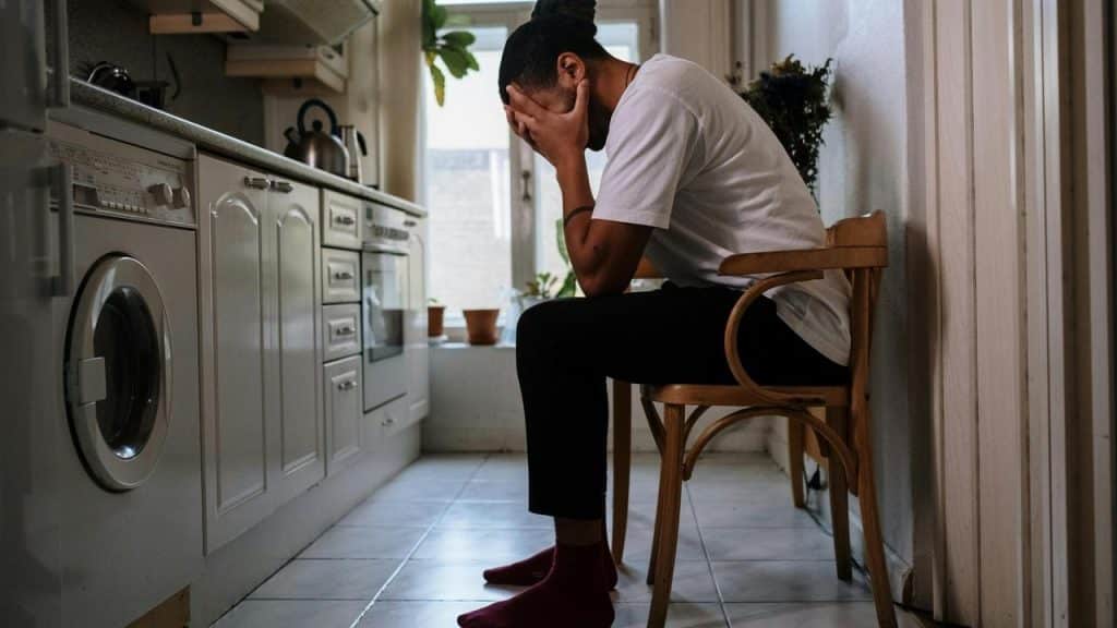 A person sitting in a kitchen with their face buried in their hands.