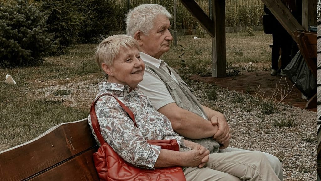 A man and a woman sitting on a wooden bench.